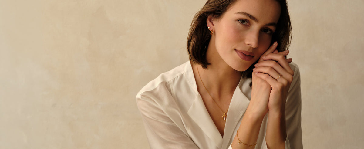 Woman wearing diamond jewelry by MILLSÉ including a 14k gold vermeil pendant necklace, diamond stud earrings, and diamond pendant bracelet from the Gifts for Her collection. 